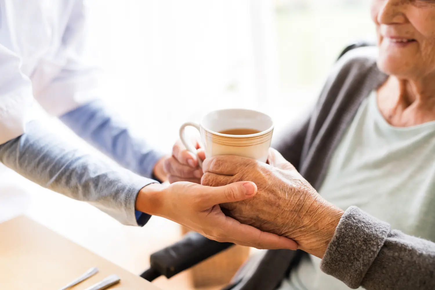 Eine Pflegekraft bietet einer älteren Person eine Tasse Tee oder Kaffee an, wahrscheinlich in der häuslichen Pflege.