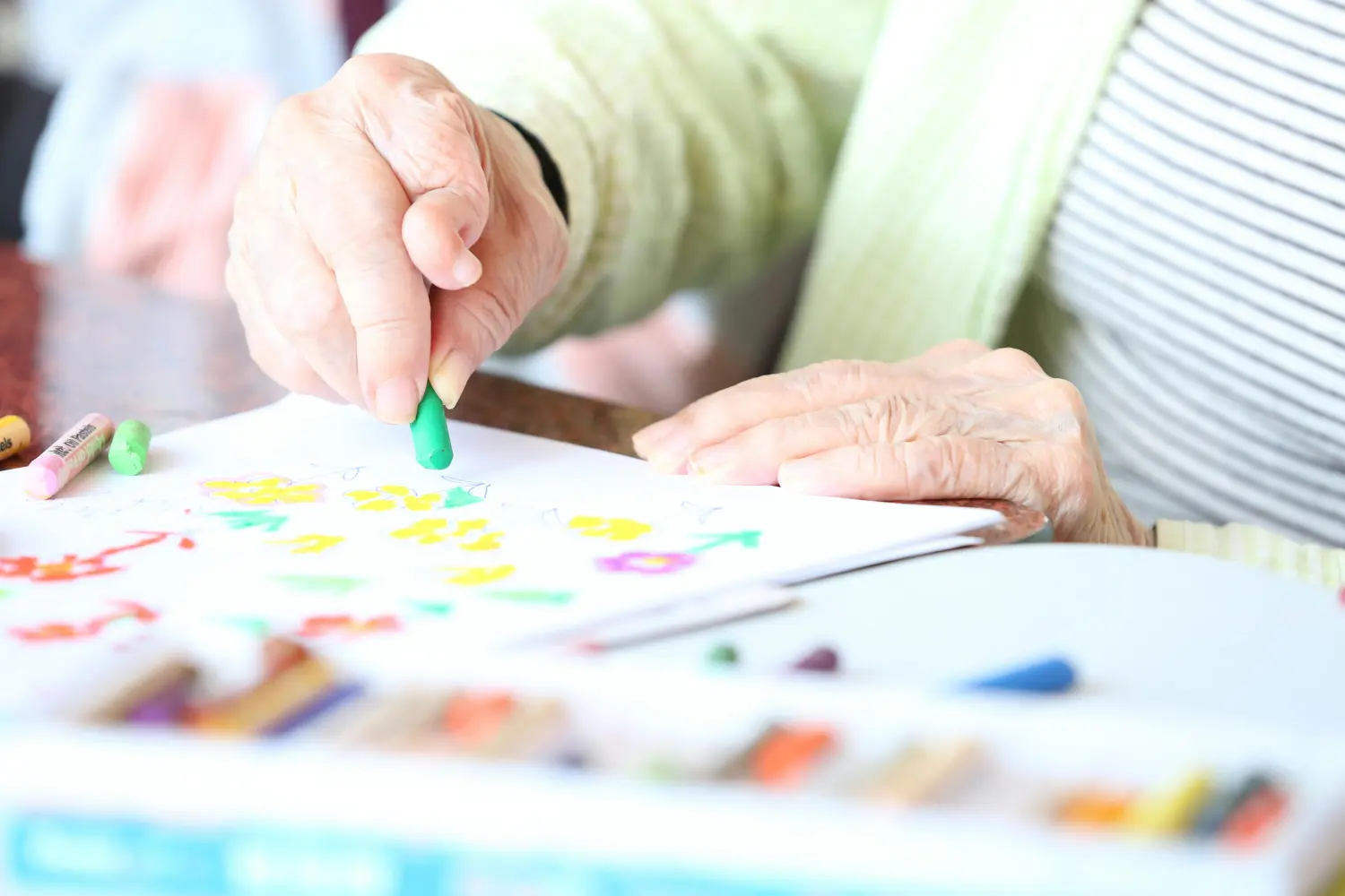 Eine ältere Person, die eine Kunsttherapie durchführt, insbesondere beim Malen mit Buntstiften. Von Weiße Elfen München Süd UG